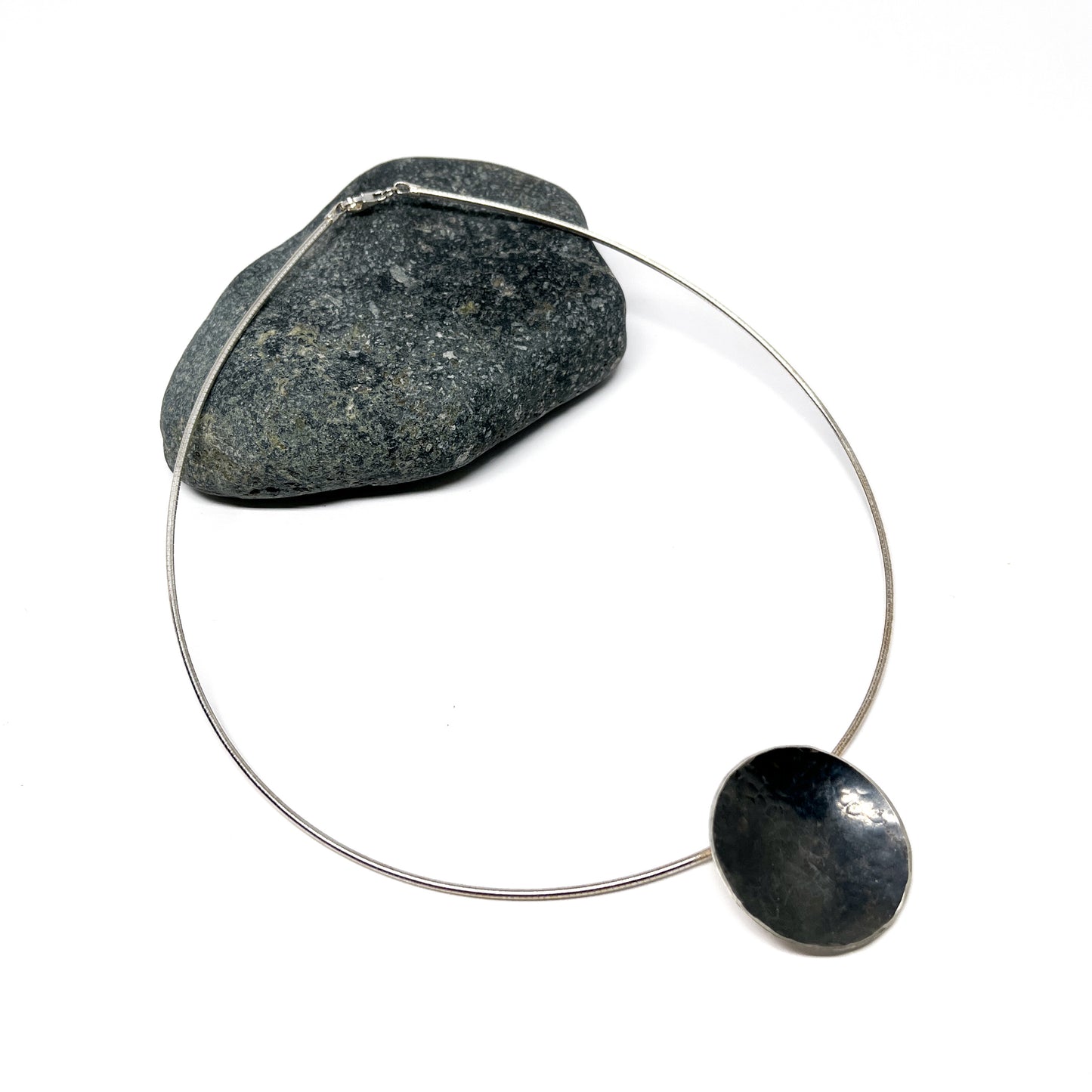 Moonspace Pendant Necklace with a dark, textured pendant next to a gray stone.