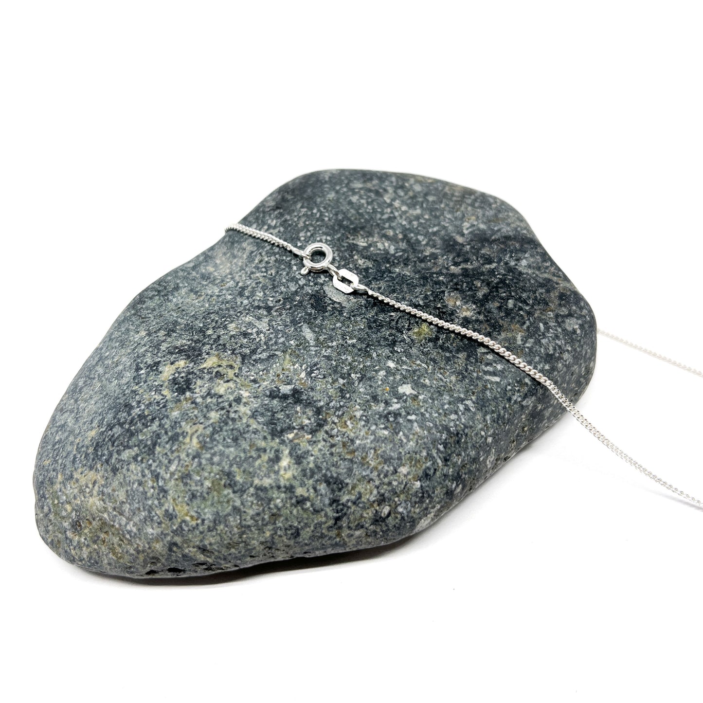 Close-up of the clasp of a silver chain necklace resting on a textured stone.