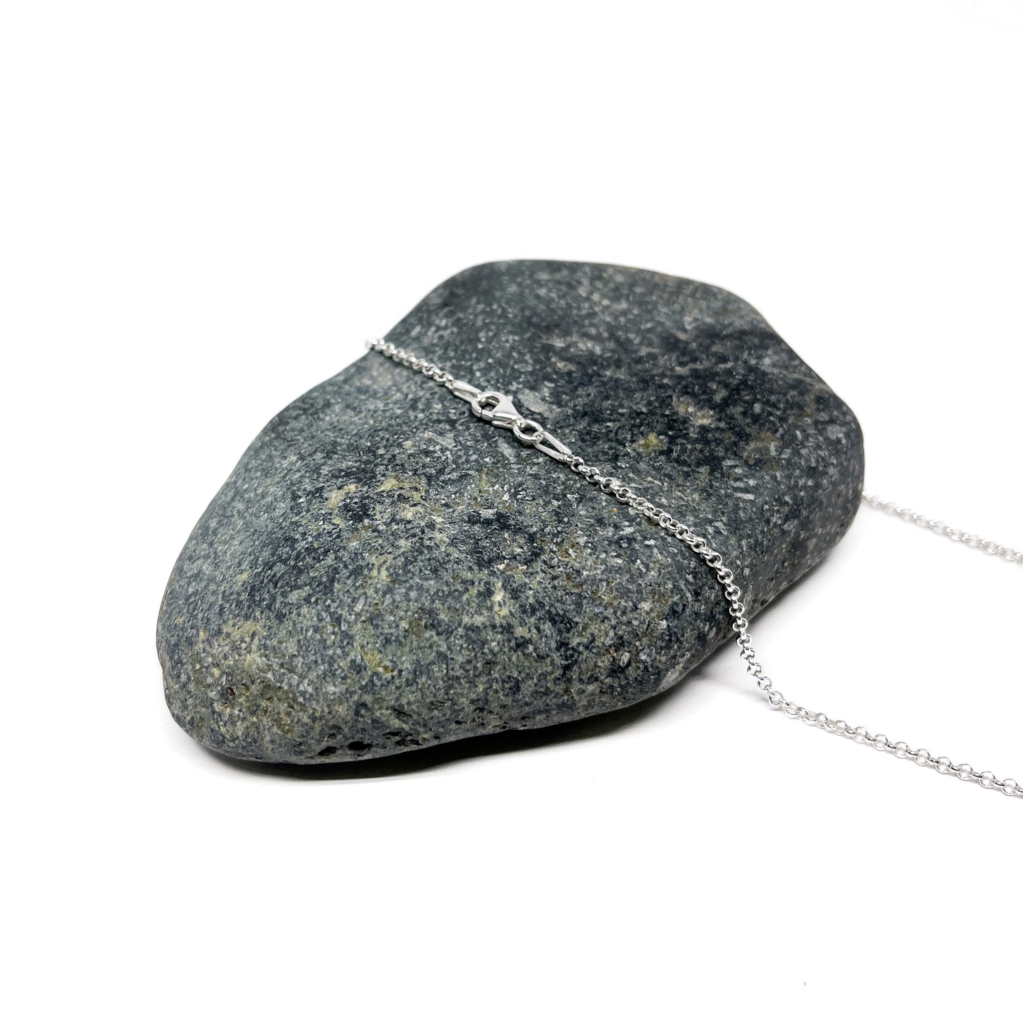 Detail of the silver chain and clasp of a loop pendant necklace on a stone.