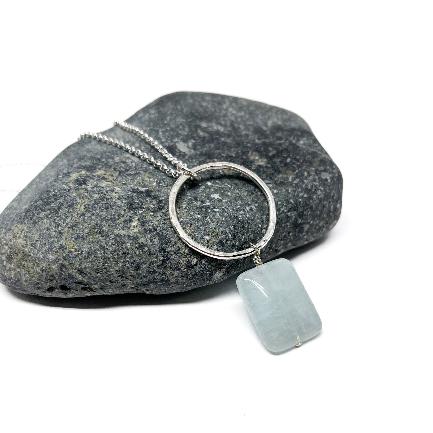 Silver loop pendant necklace with a pale blue rectangular gem, on a stone.