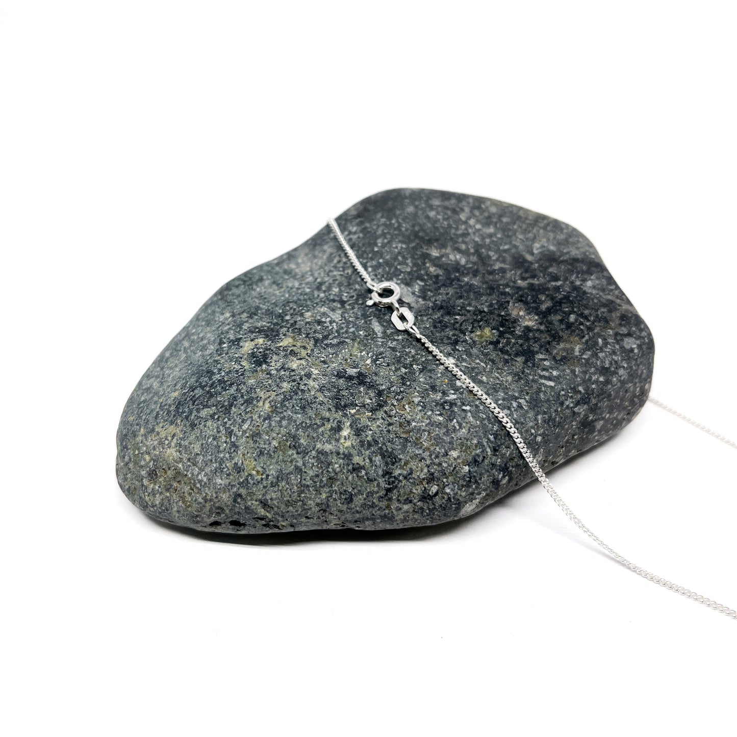 The clasp of a silver chain necklace with a loop and pearl pendant, shown on a stone.