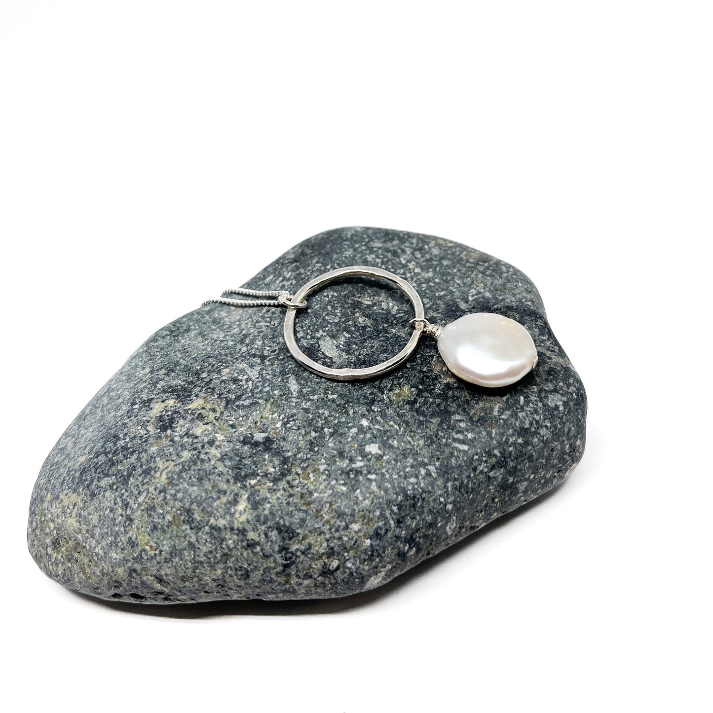Close-up of a silver necklace with a circular loop and a unique, flat baroque pearl.