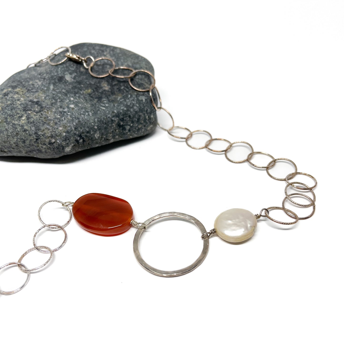 Close-up of a carnelian, silver loop, and pearl on a silver chain.