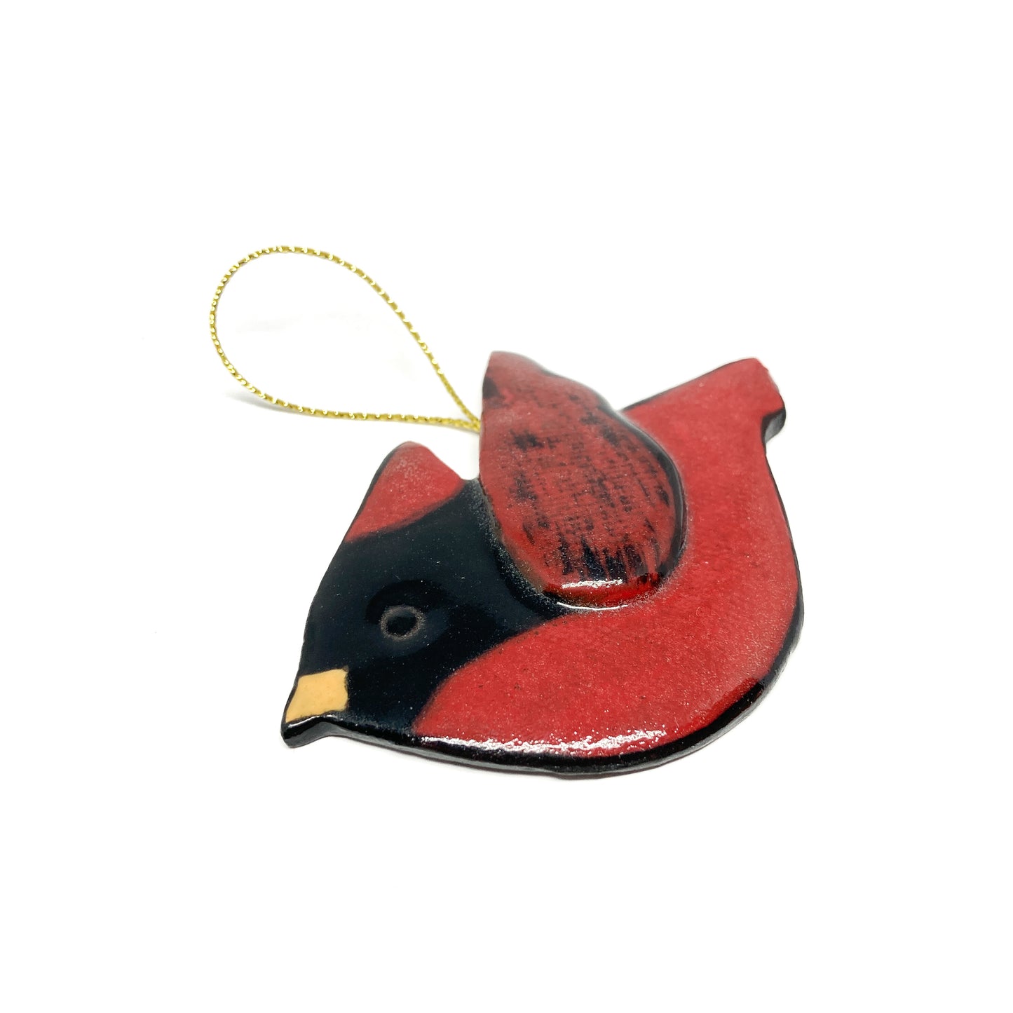 A red bird ornament with dark wings and a gold string, viewed from a low angle.