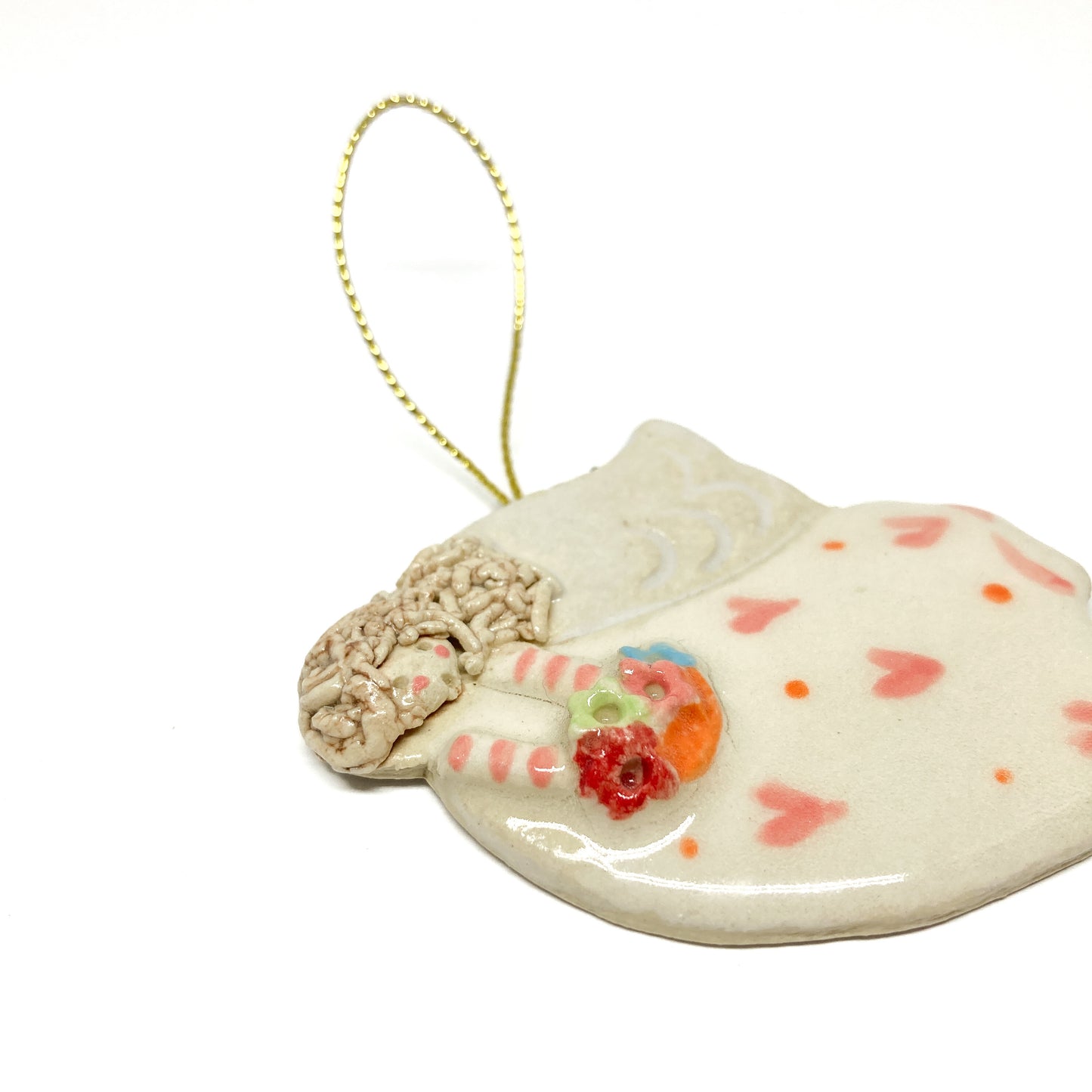 A white angel ornament with pink hearts, striped sleeves, and a gold string.