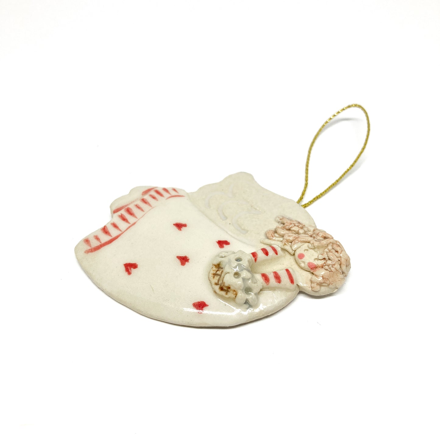 A white angel ornament with pink hearts, striped sleeves, and a gold string.
