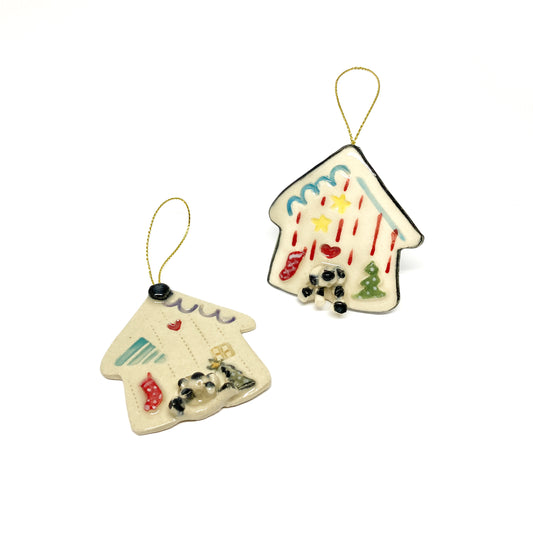 Two house-shaped ornaments with Christmas decorations and gold strings.