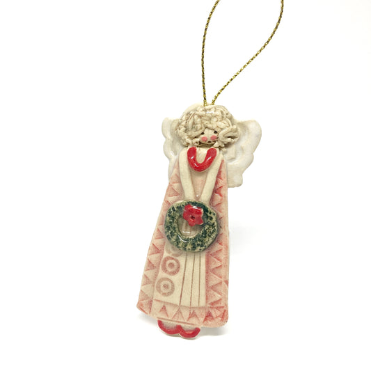 A white angel ornament with a wreath, red accents, and a gold string.