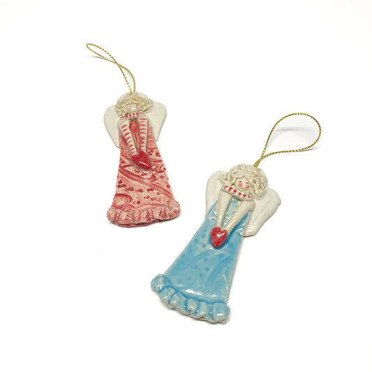 Two angel ornaments with hearts and gold strings, one pink and one blue.