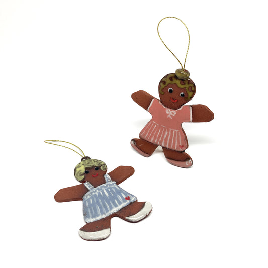 Two gingerbread girl ornaments with dresses and gold strings.