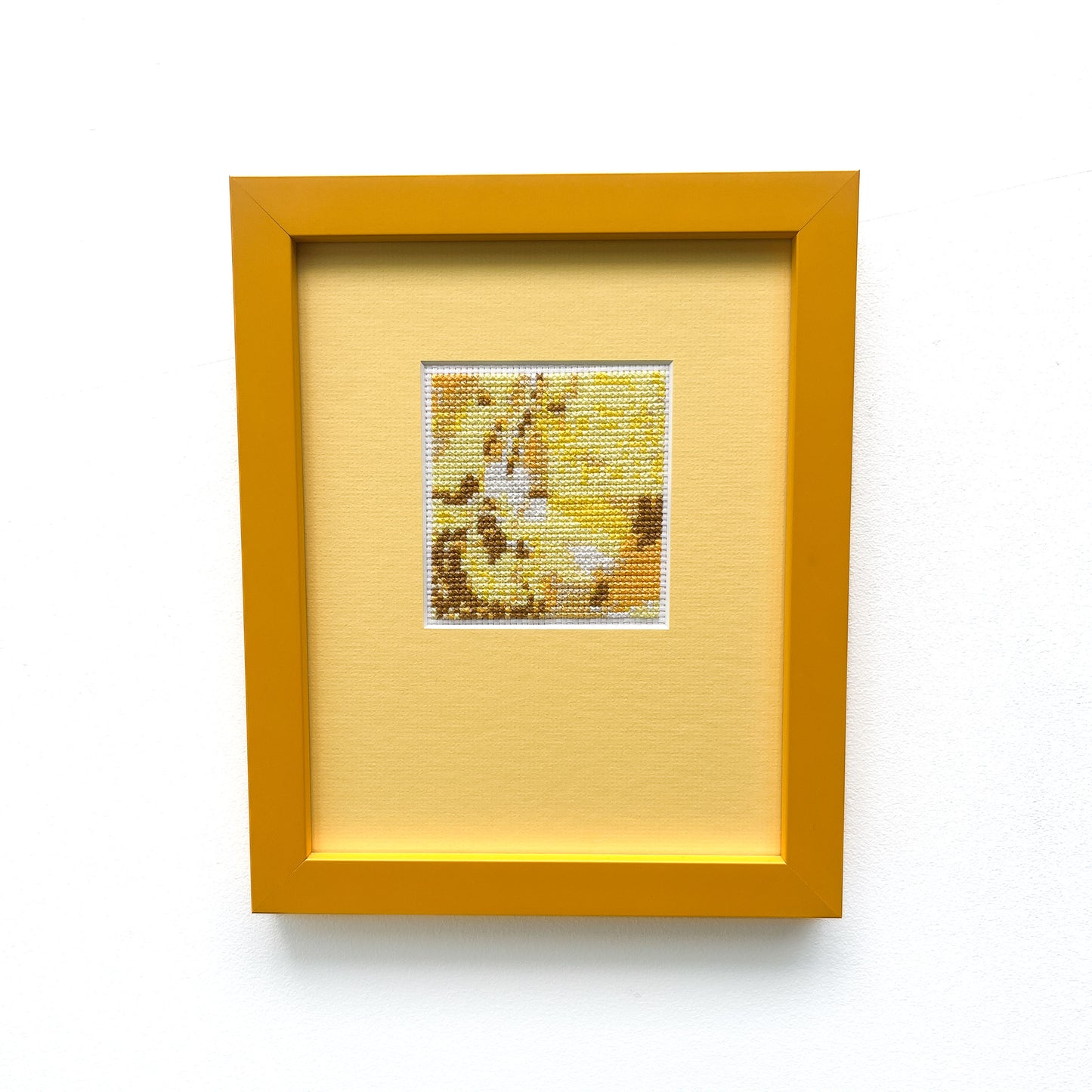 Framed "Yellow Monochrome" cross-stitch. A small square of stitched art is centered on a larger yellow mat within a yellow frame.