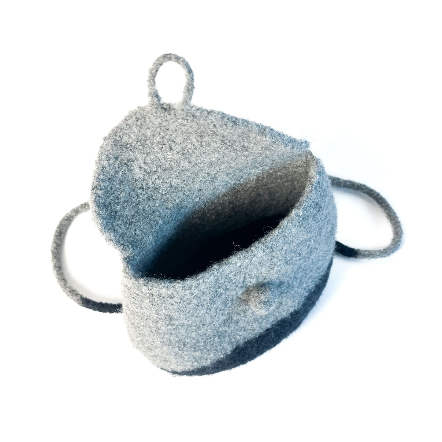 Open, two-tone felted backpack with a button detail and thin shoulder straps, showing the interior.
