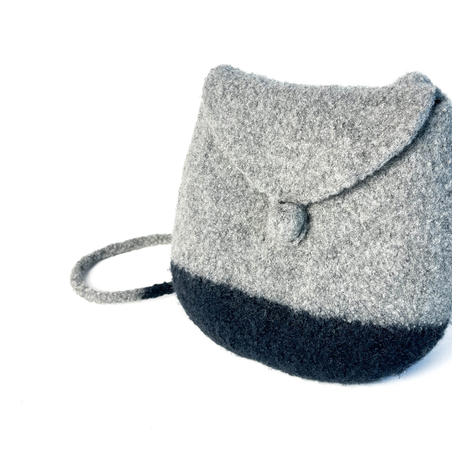 Close-up of a two-tone felted backpack with a flap closure and button detail. A thin shoulder strap is visible.