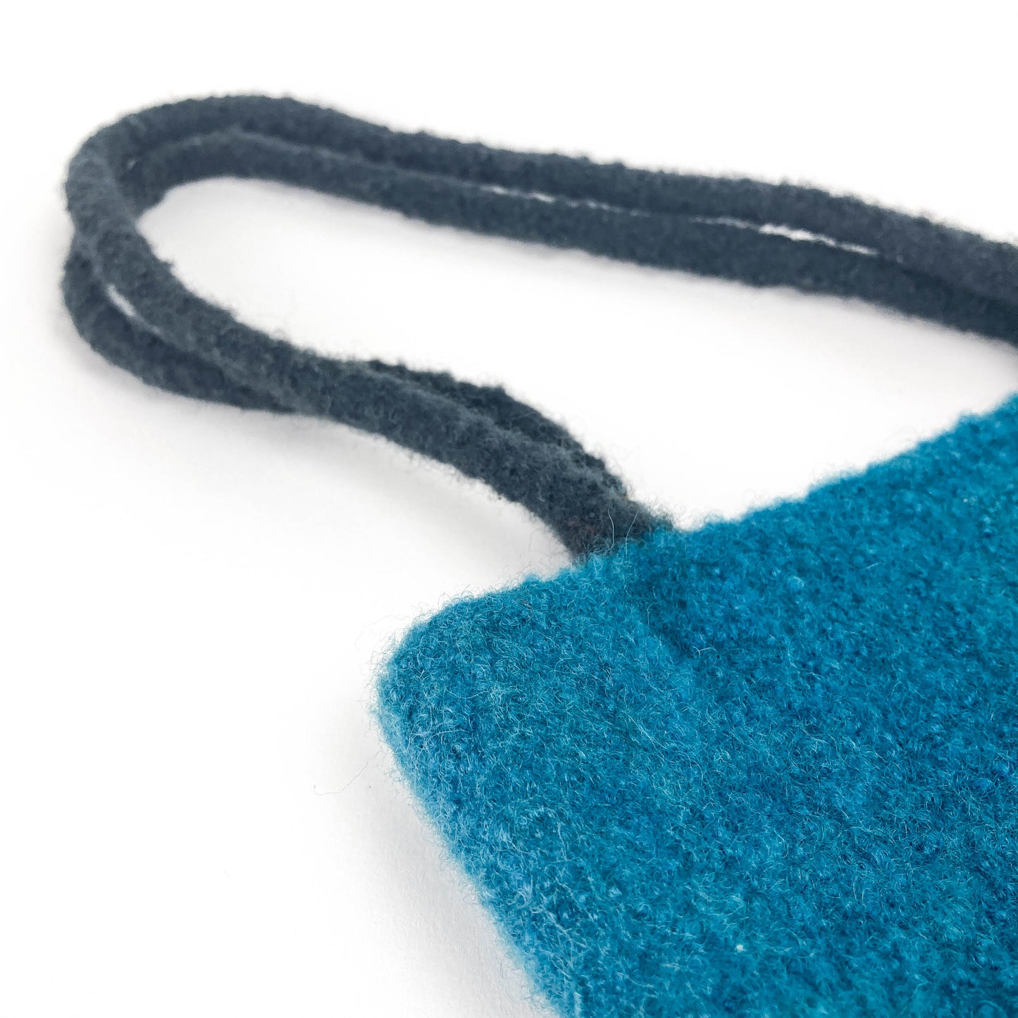 Close-up of a vibrant colored felted bag with thick, dark looped handles. The texture of the felt is visible.