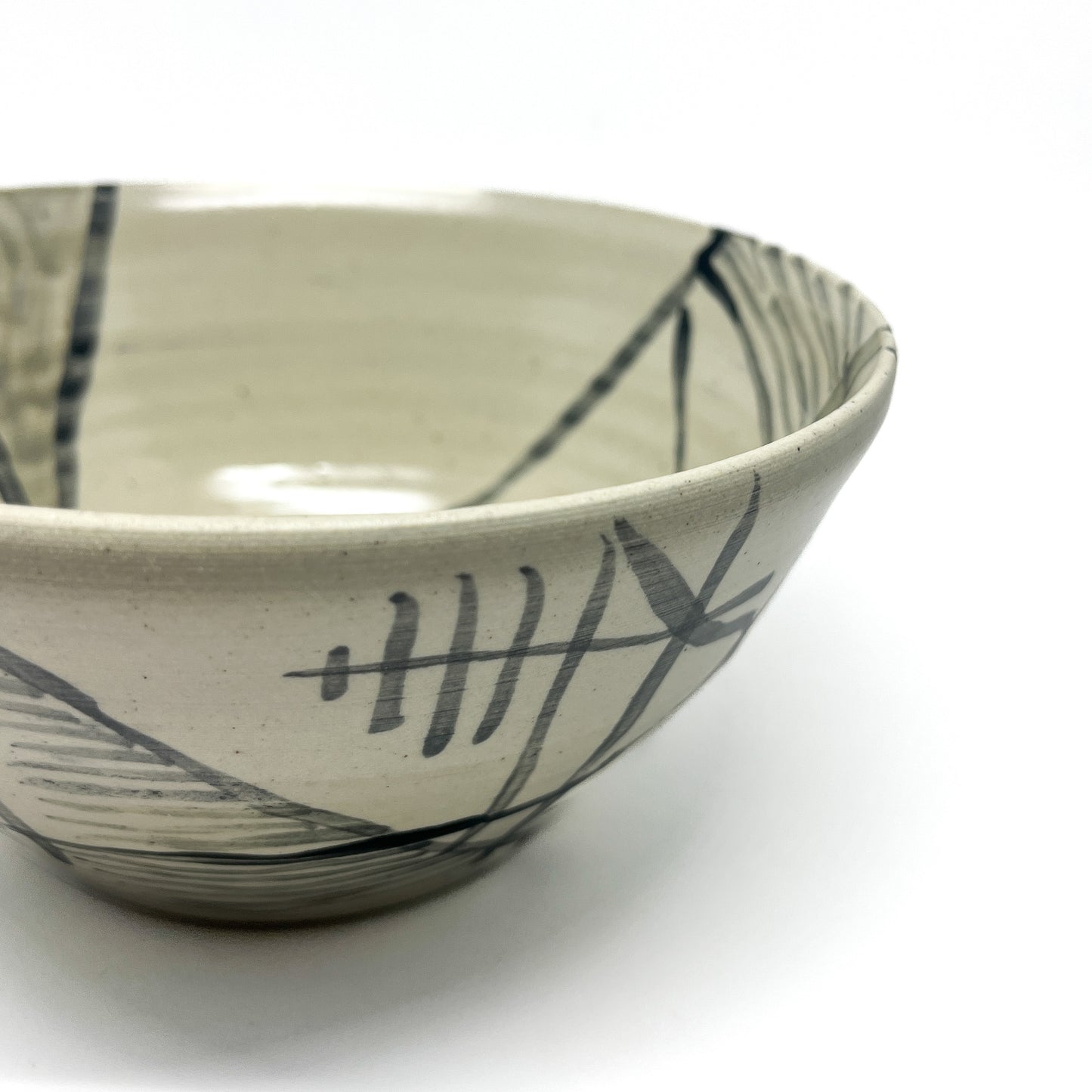 Close-up of a textured Seto-style tea bowl with abstract, dark linear and brushstroke patterns.