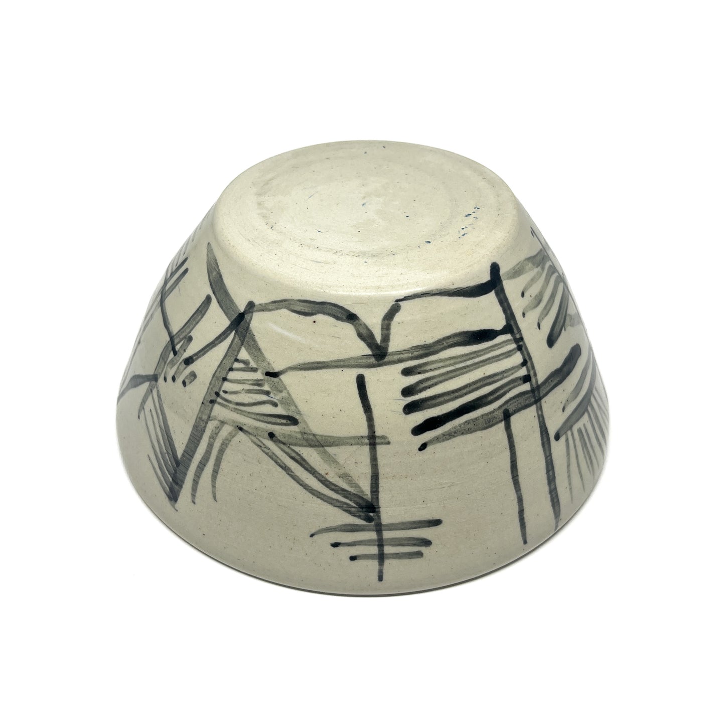 Bottom view of a textured ceramic tea bowl with abstract, dark painted lines and brushstrokes.