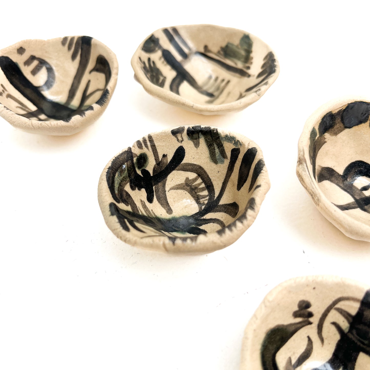 Five small, handmade ceramic bowls, each featuring unique black abstract patterns.