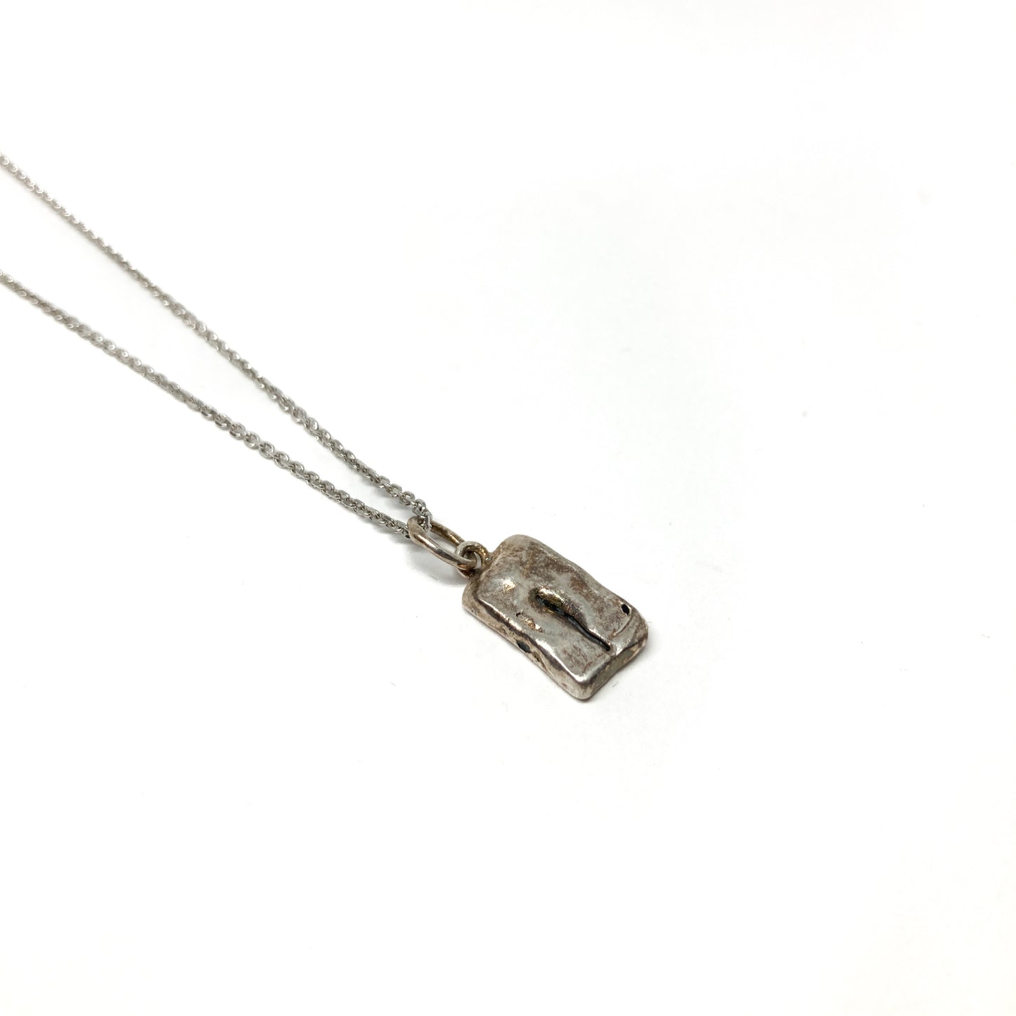 Single small silver pendant with an abstract etched design on a delicate chain.