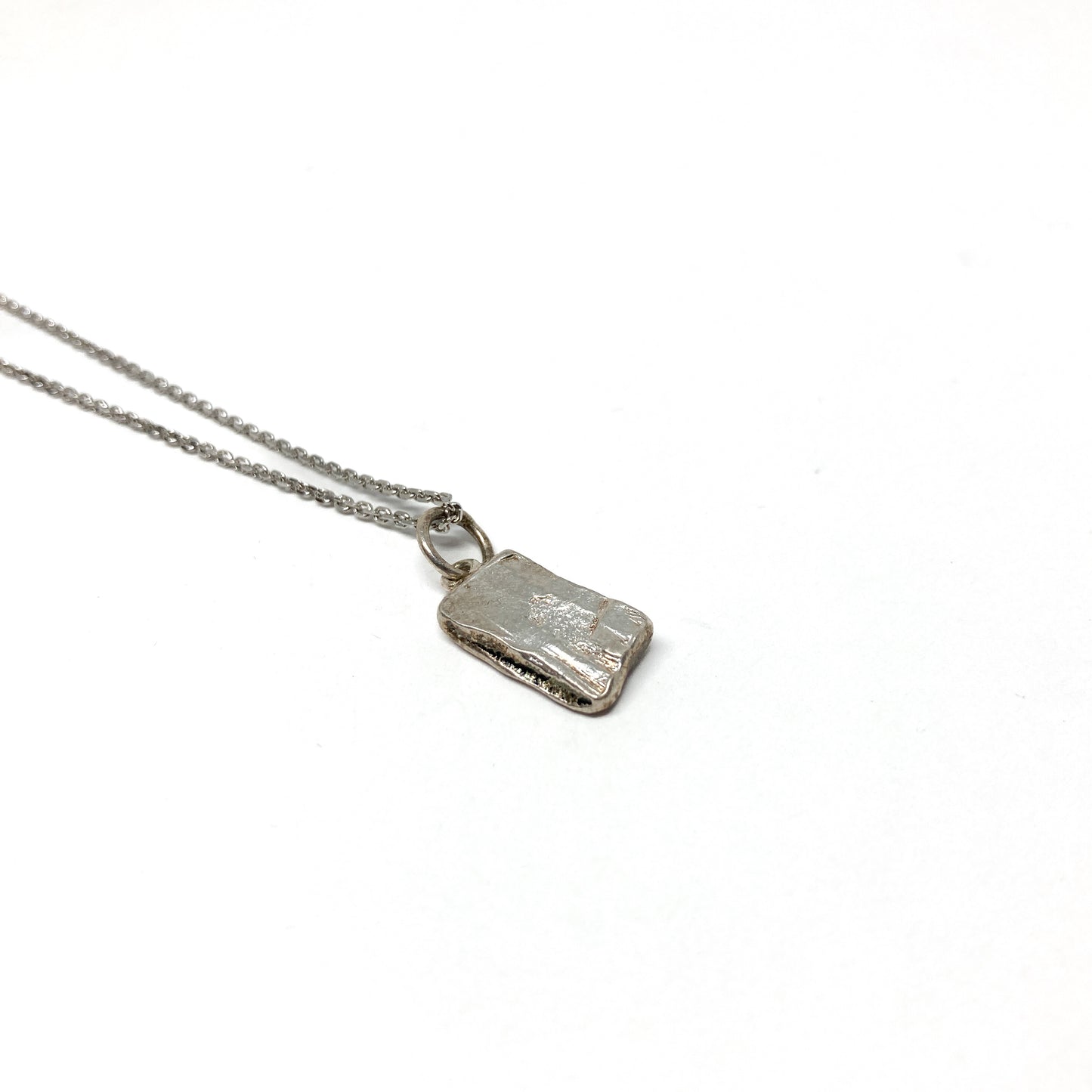 Back view of a small silver pendant revealing its smooth, unadorned surface.