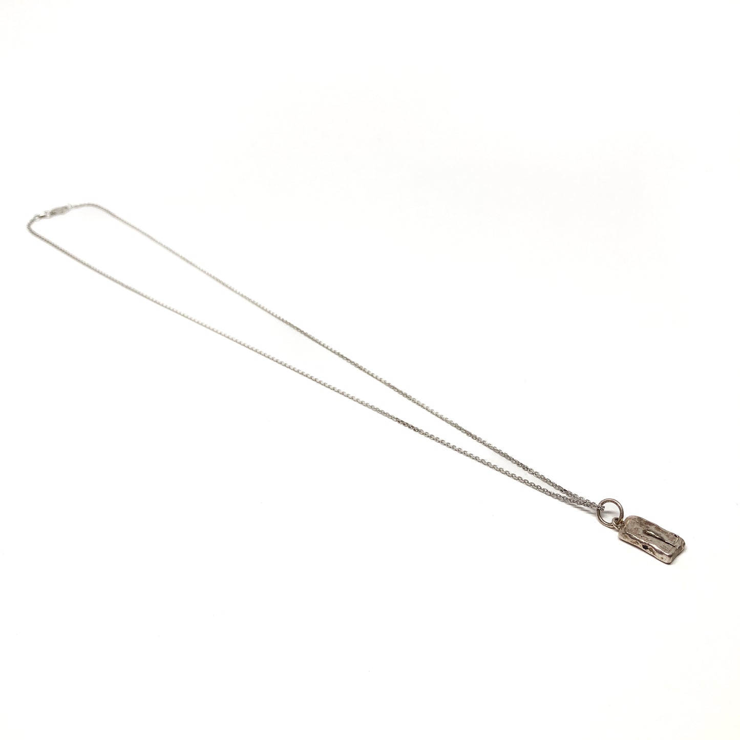 Angled view of a small silver pendant necklace lying on a plain surface.