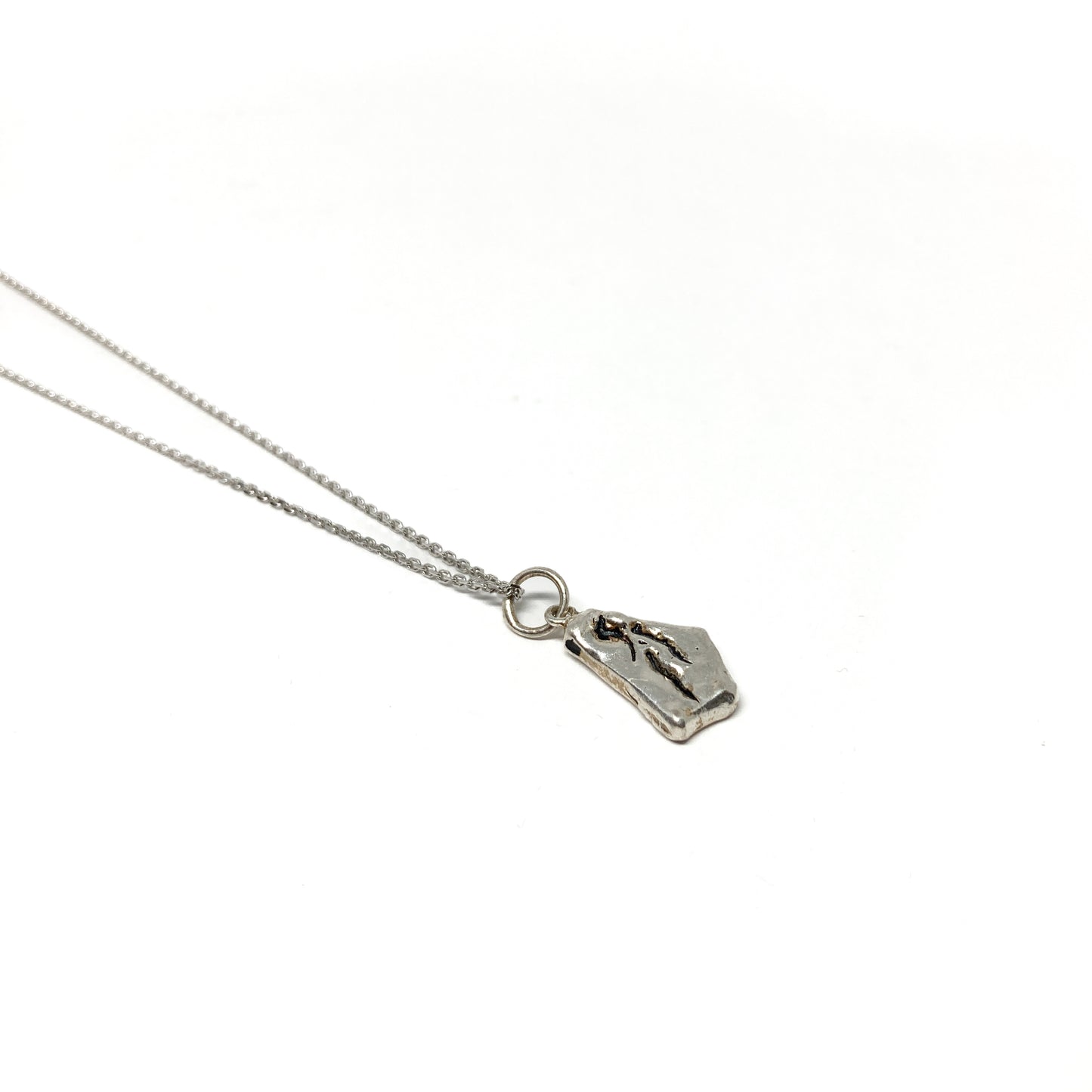 Close-up of a small silver pendant with a distinct abstract pattern and chain.