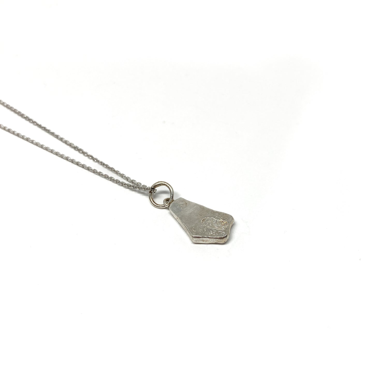 Reverse angle of a small silver pendant showing its simple, solid backing.