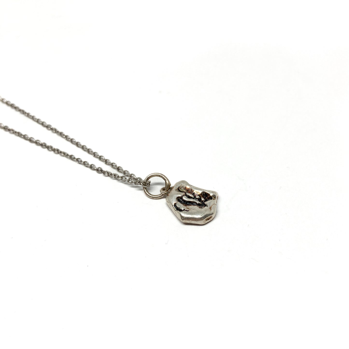 Detailed shot of a small, organically shaped silver pendant with dark accents.