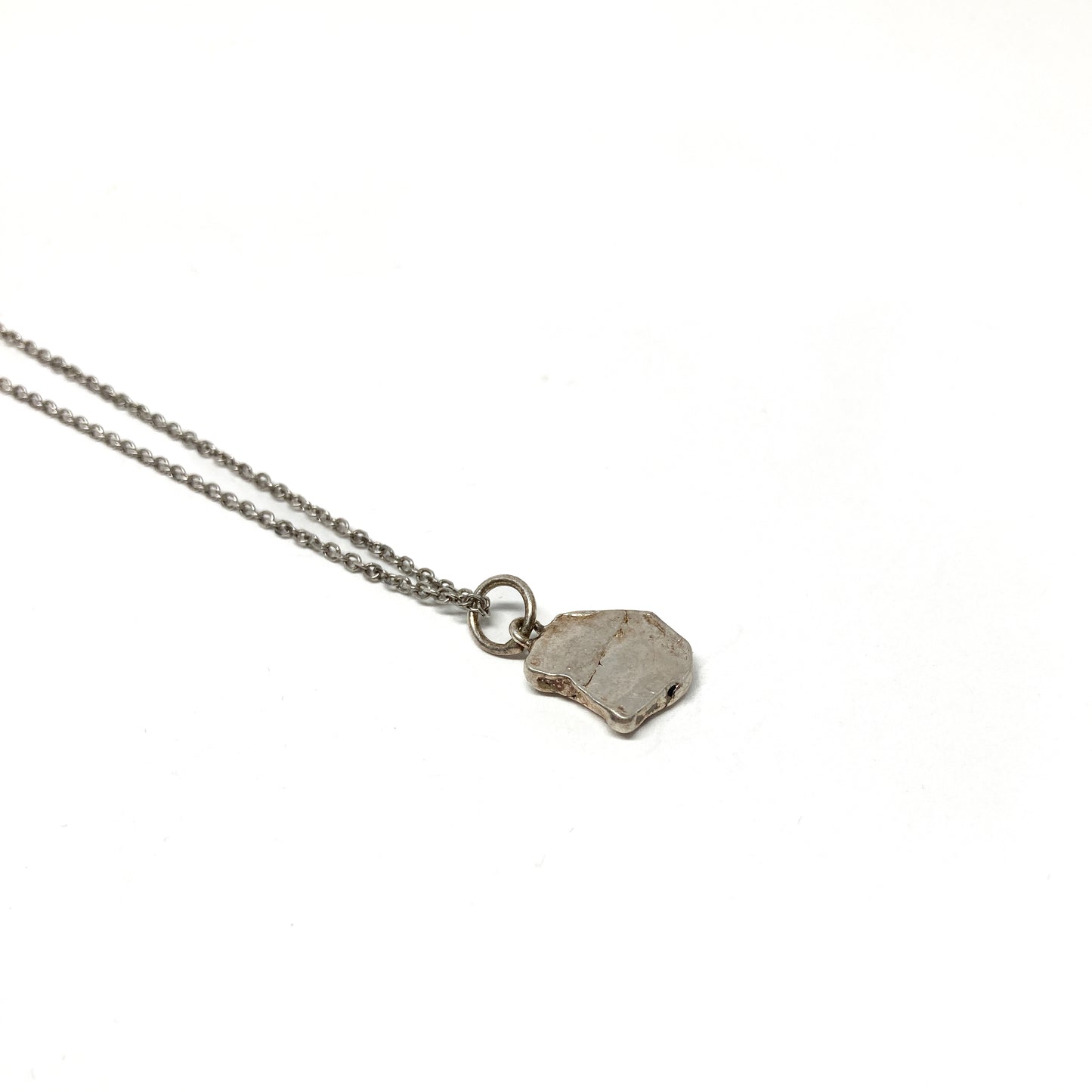 Backside detail of a small silver pendant on a fine chain.