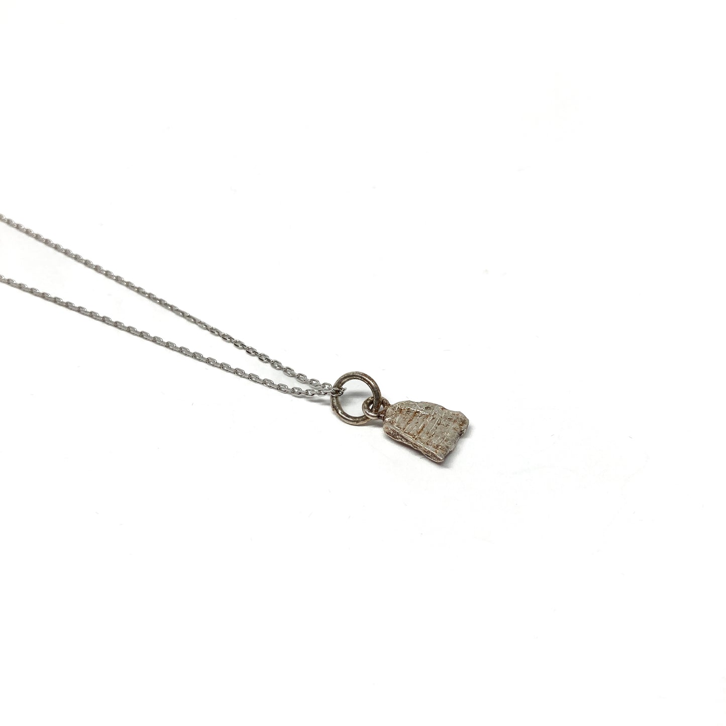 Detailed view of a small silver pendant with an organic shape.