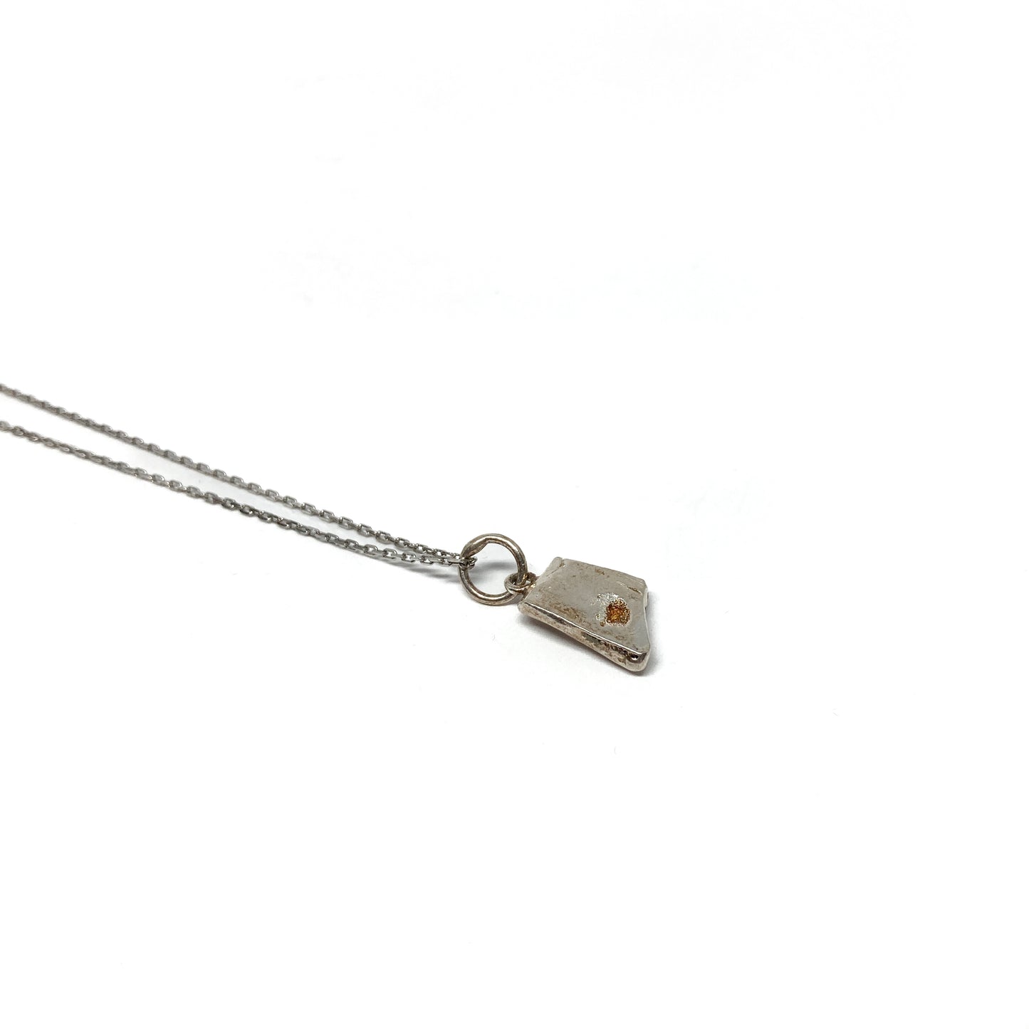 Side view of a small silver pendant showing its texture.