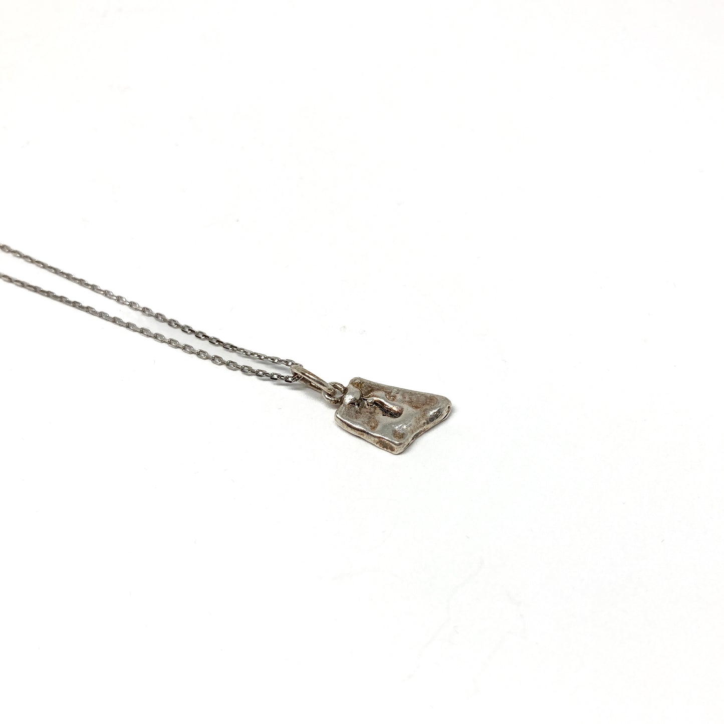 Angled close-up of a unique, small silver pendant.