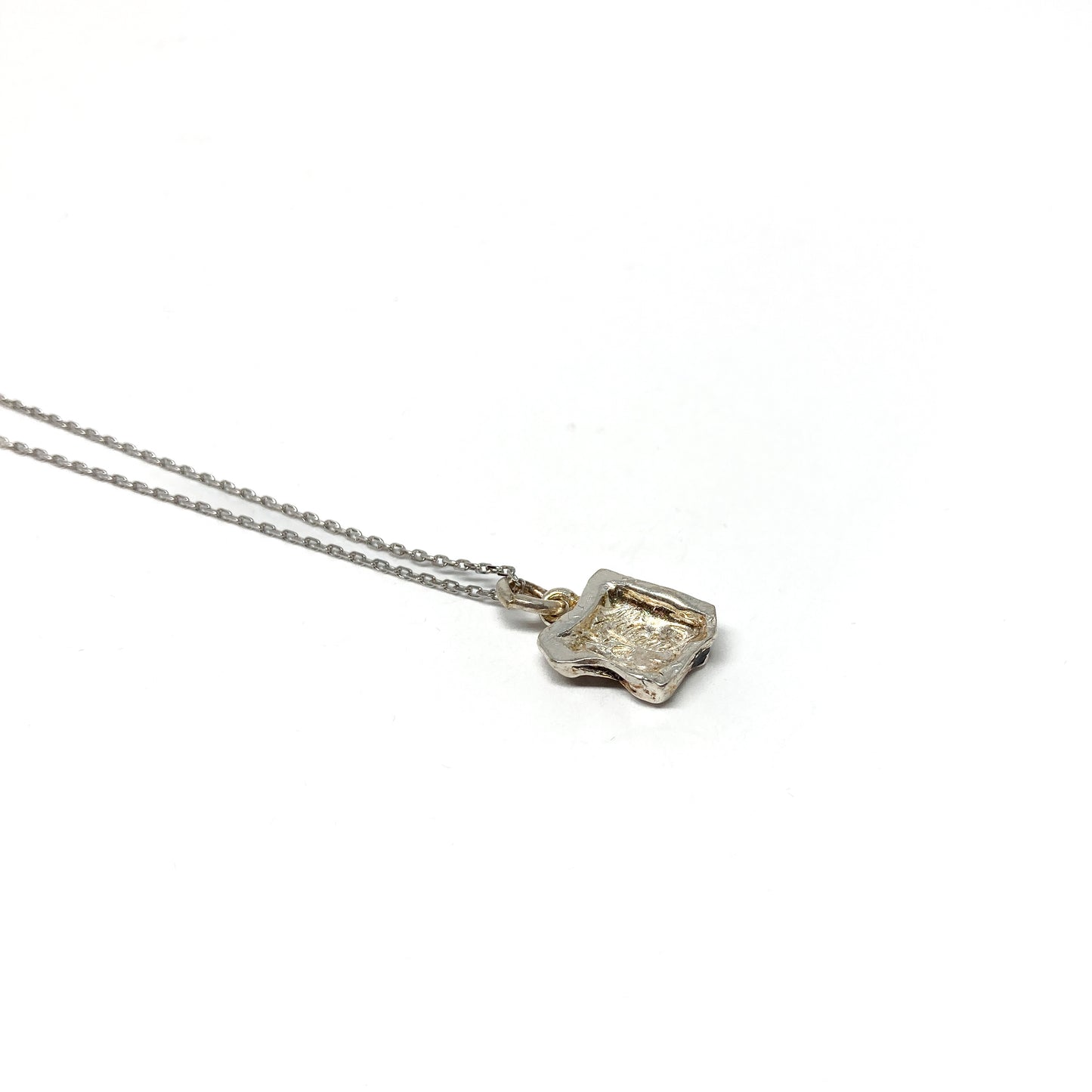 Back view of a small, irregularly shaped silver pendant.