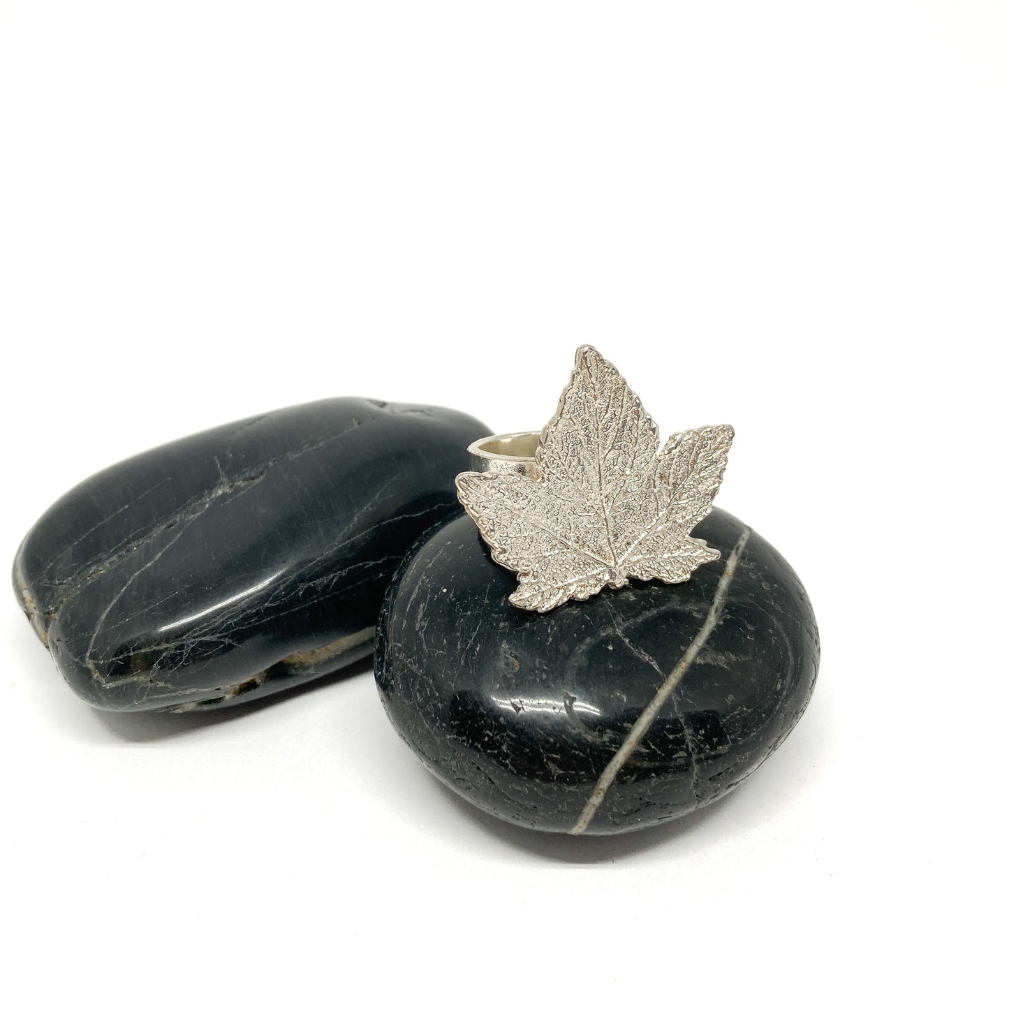 Silver maple leaf ring on a smooth, dark stone with another stone beside it.