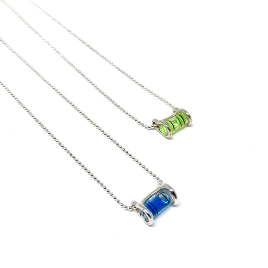 Two silver necklaces with cylindrical glass pendants containing swirling green and blue pigments, appearing like miniature levels.