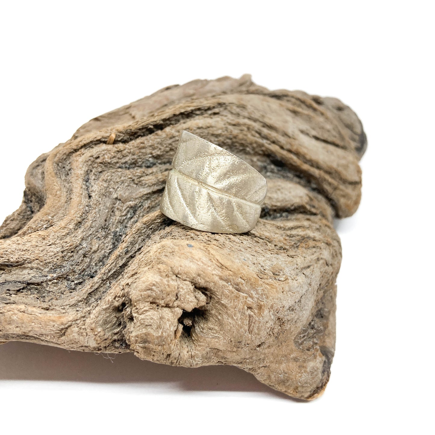 Textured silver ring with a leaf-like design, resting on a piece of weathered driftwood.