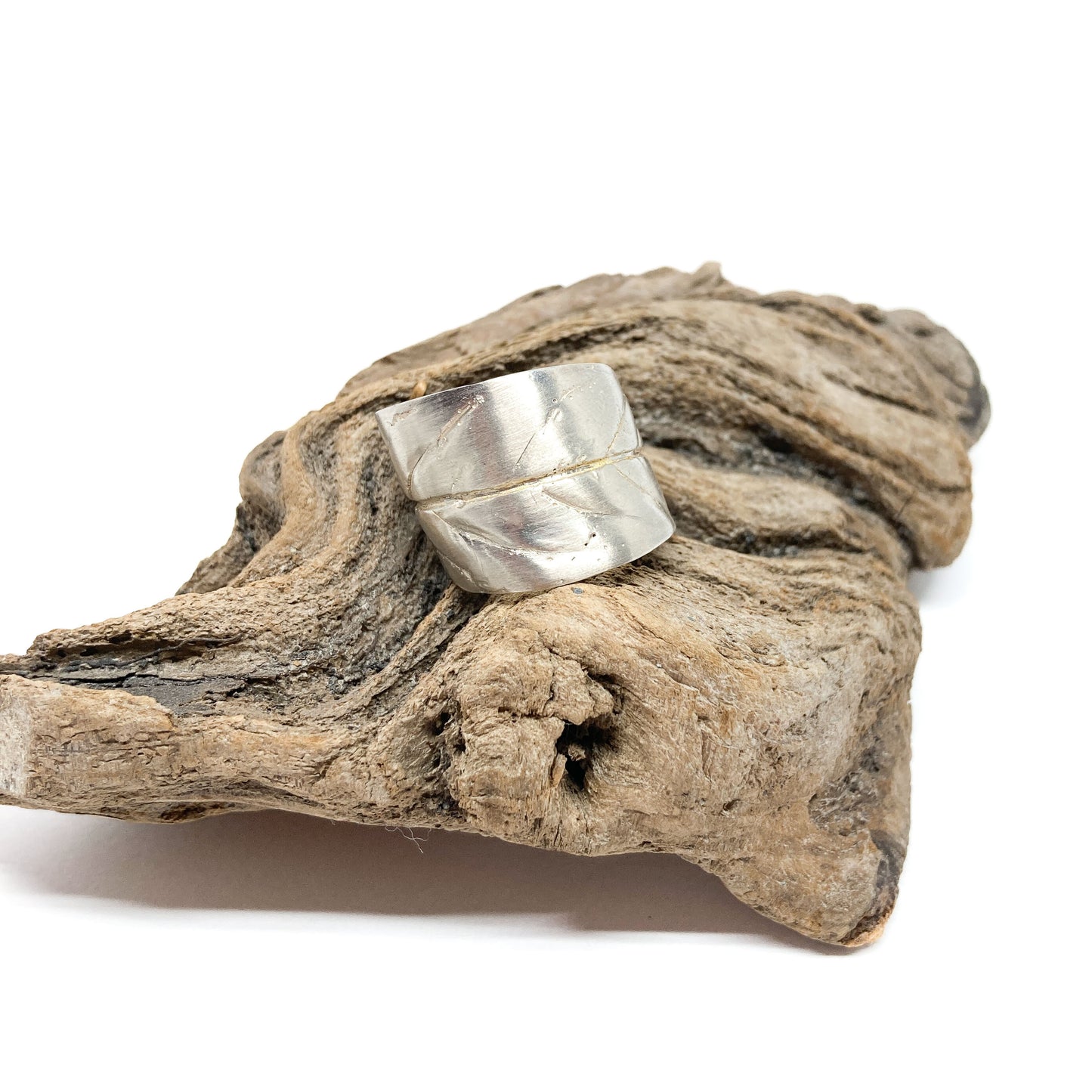 Textured silver ring with a stylized leaf design, resting on a piece of weathered driftwood.