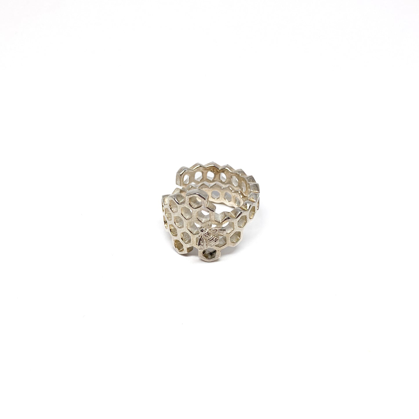 A shiny silver ring shaped like a honeycomb wraps around, featuring a detailed bee on one cell.