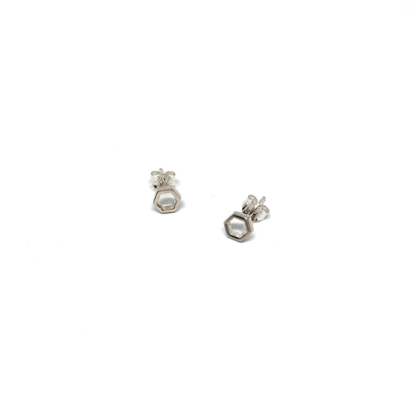 Two shiny silver stud earrings, each shaped like a small, open hexagon, are displayed.