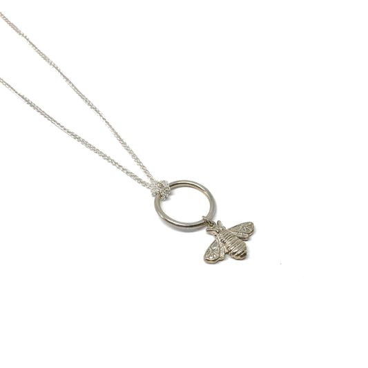 A delicate silver necklace features a circular pendant with a detailed bee charm dangling from it.