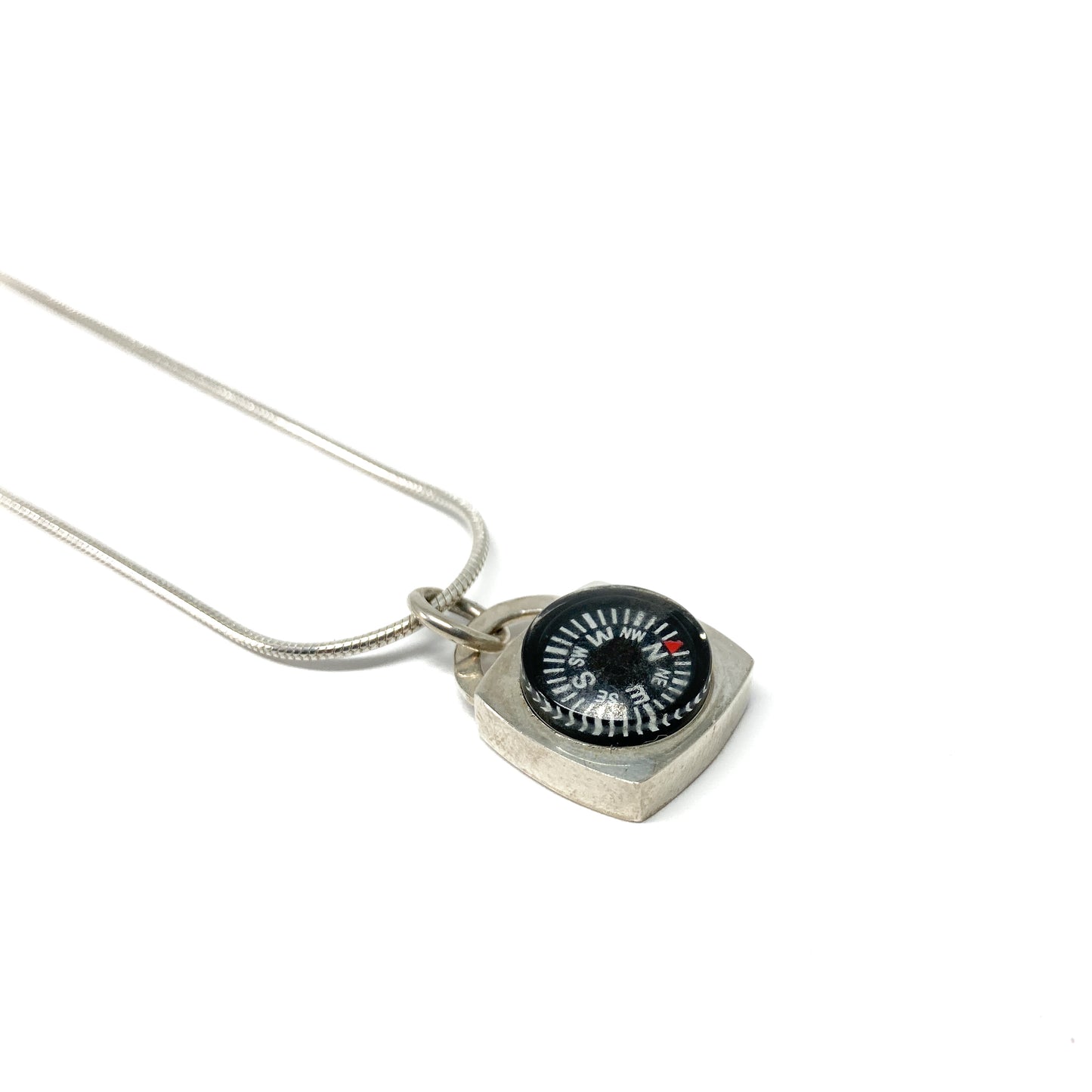 A silver necklace features a square pendant holding a small, functional compass with visible cardinal directions.