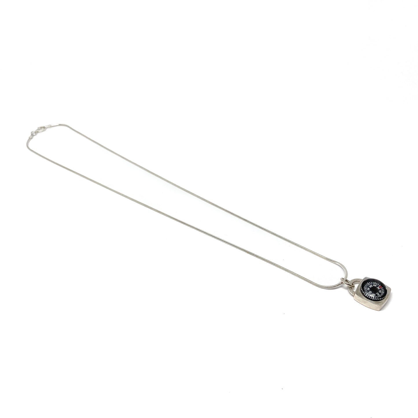A long silver necklace features a square pendant containing a small compass at the bottom right.
