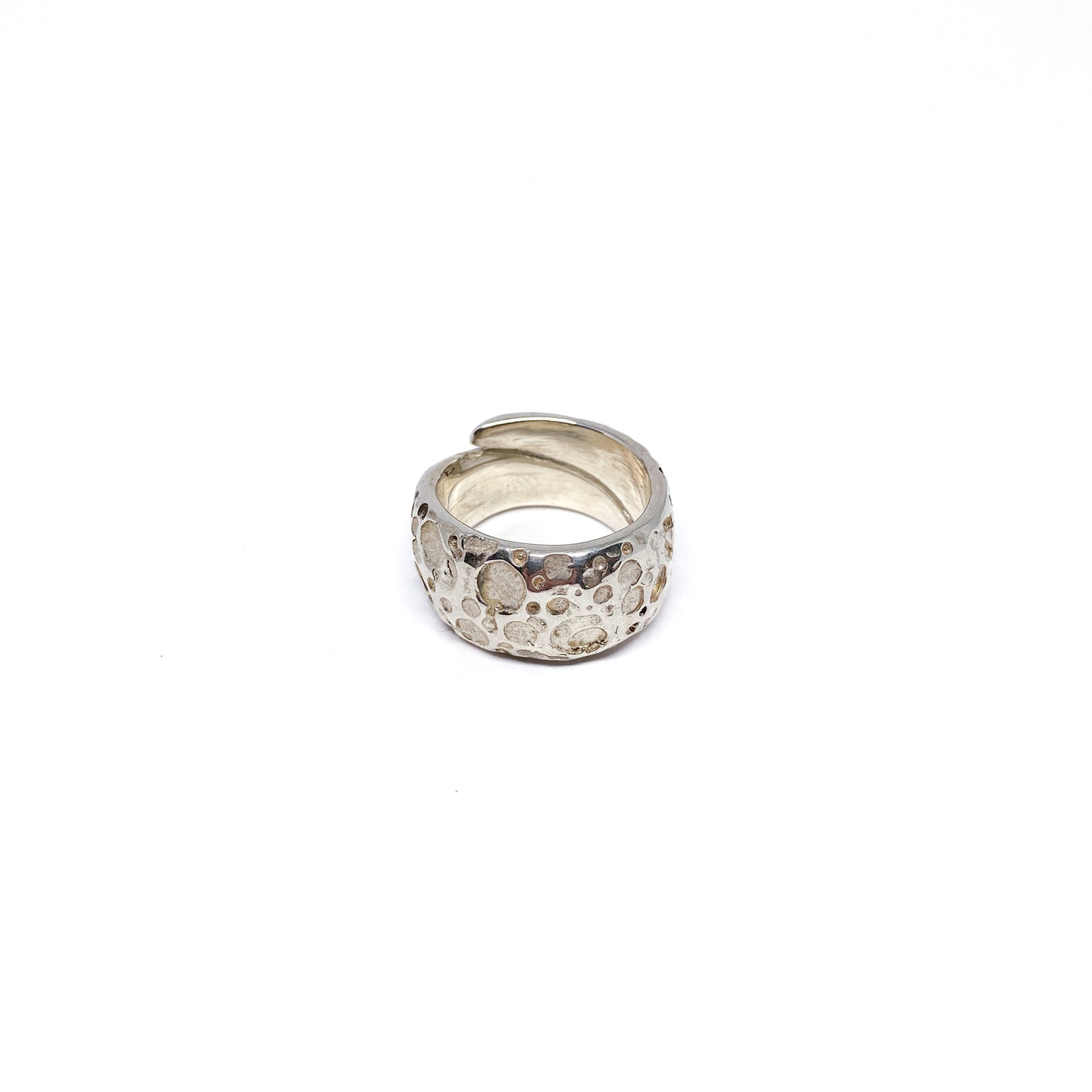 A wide band ring made of textured sterling silver with irregular indentations wraps around.