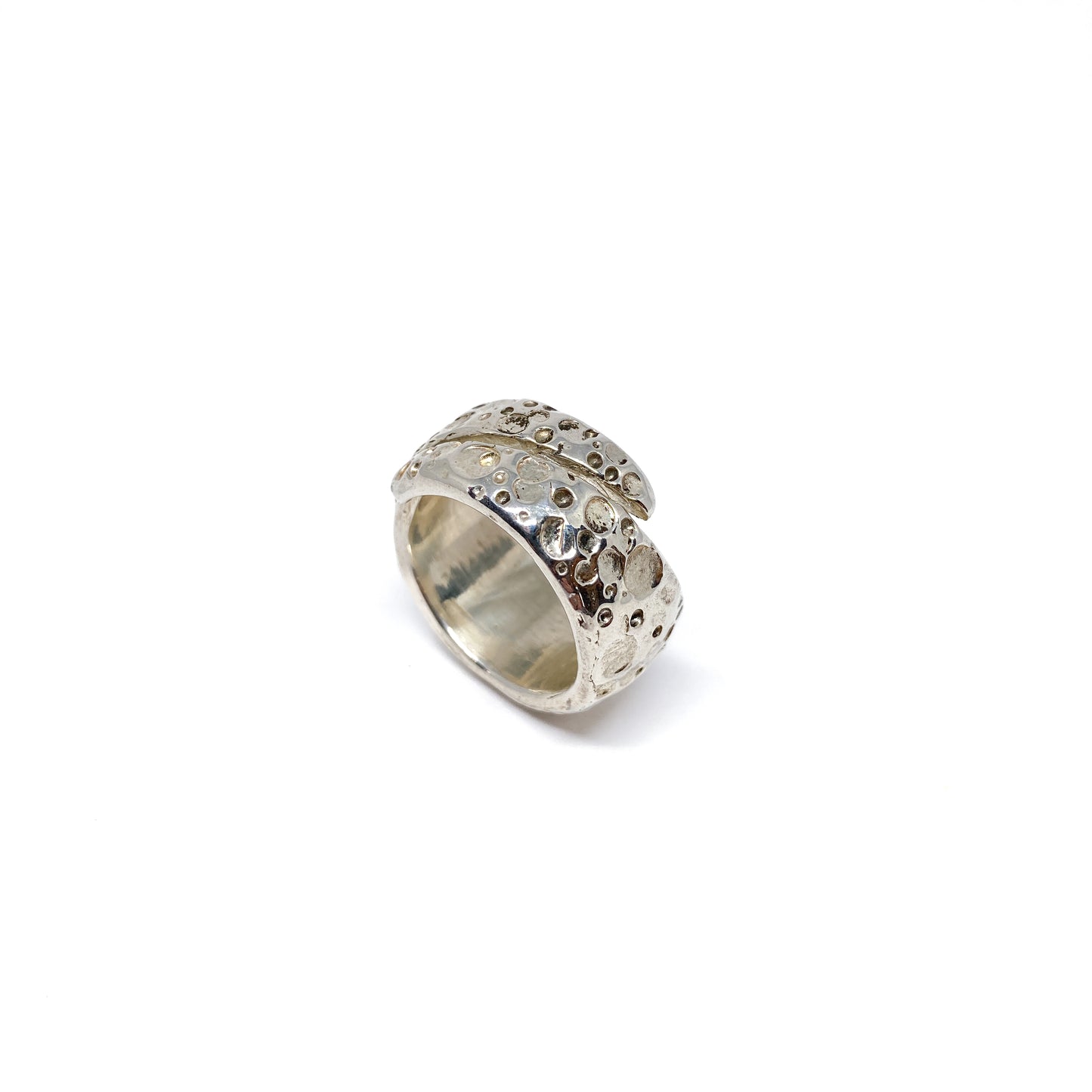 A wide, shiny silver ring with a textured surface featuring crater-like indentations wraps around.