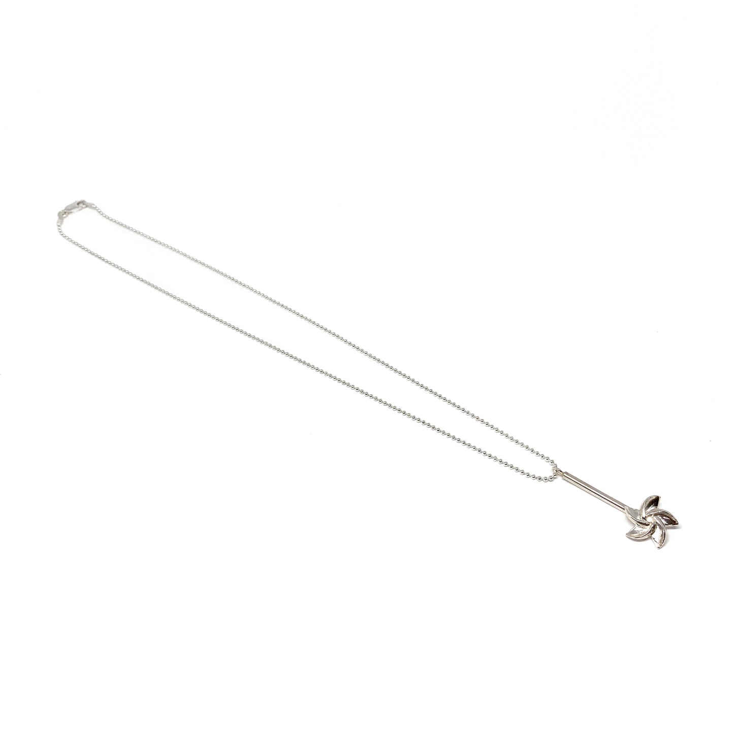 A long silver ball chain necklace features a pendant with a bar and a stylized floral or pinwheel design at the bottom.