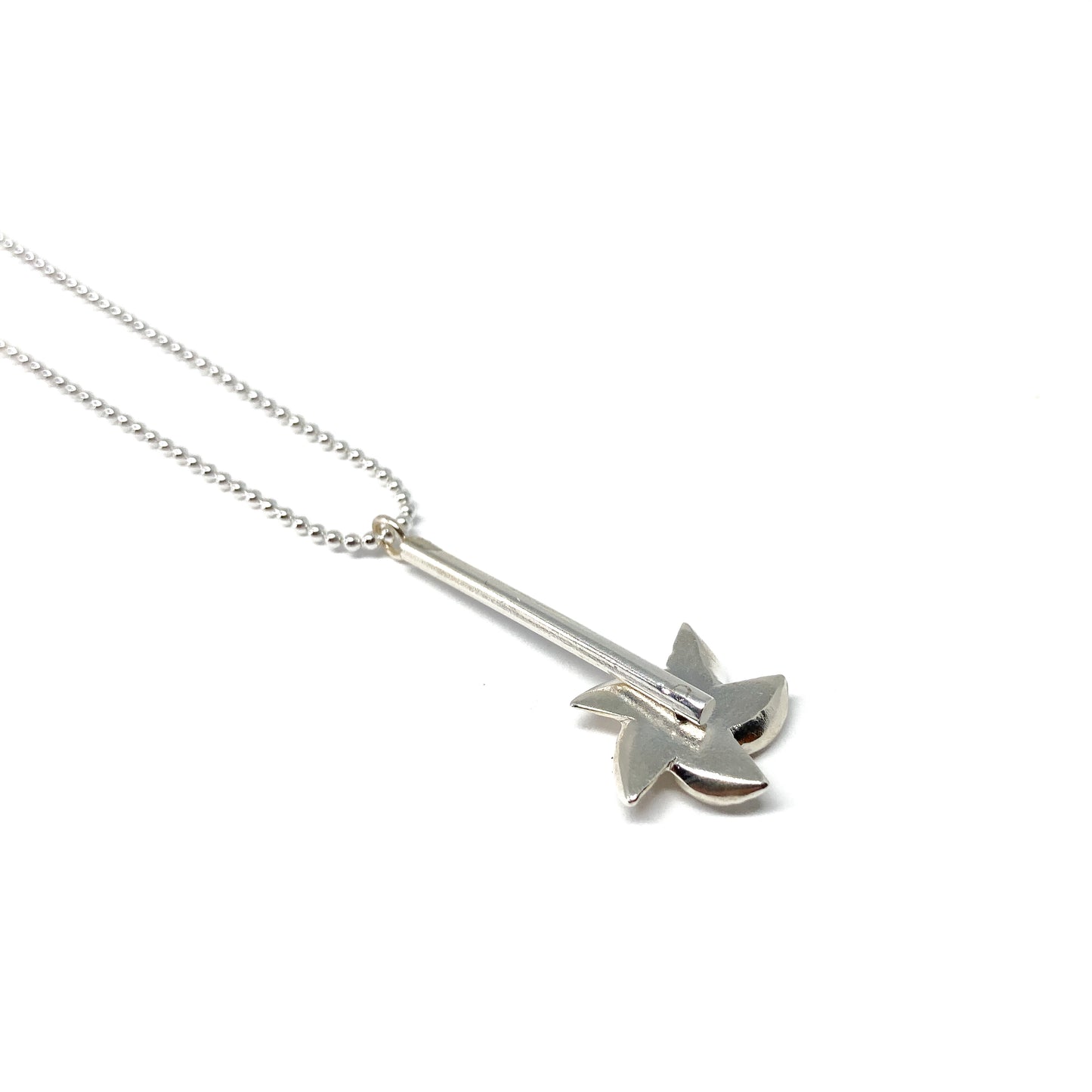 A silver ball chain necklace features a pendant with a bar and a stylized, swirling floral or pinwheel design.