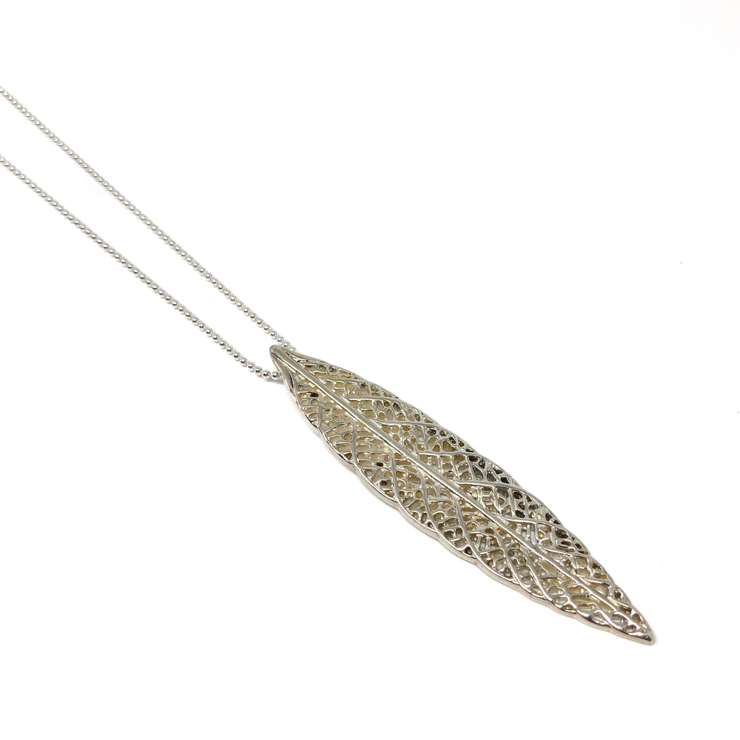 A delicate silver necklace features a long, slender pendant with an intricate, lace-like leaf design.