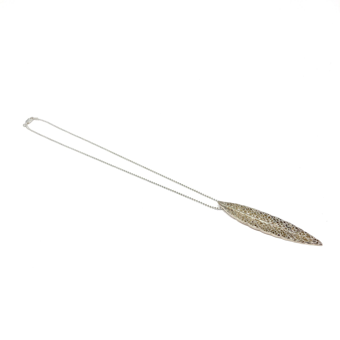 A long silver necklace features a delicate, elongated leaf-shaped pendant with an intricate openwork design.