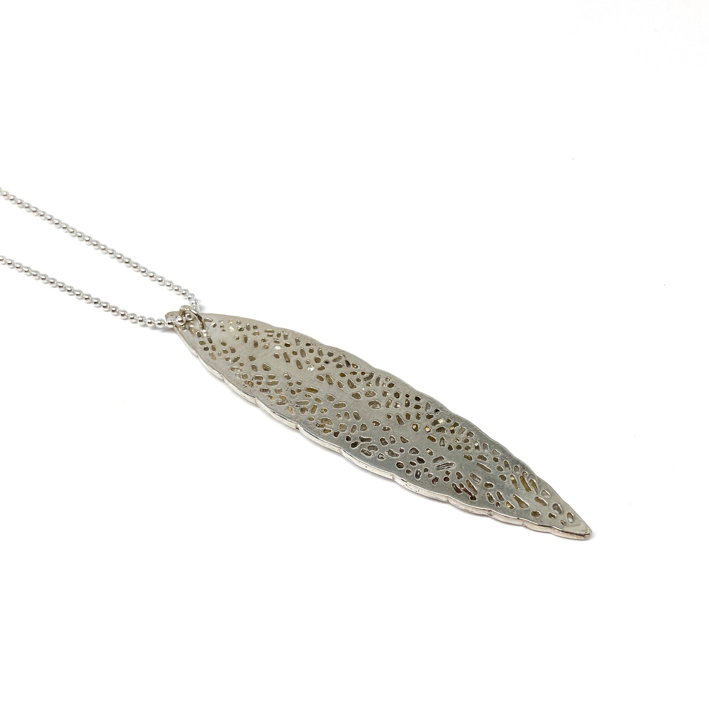 A silver ball chain necklace features a long, slender pendant with an intricate, lace-like leaf design.