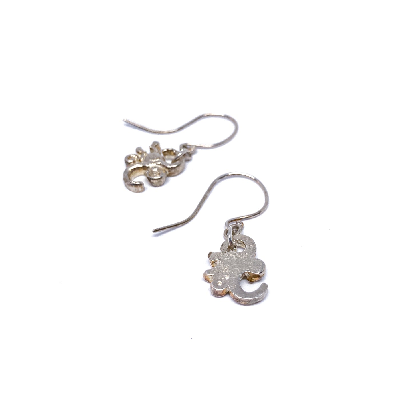 Two shiny silver dangle earrings with charms resembling stylized monkeys hang from fishhook wires.