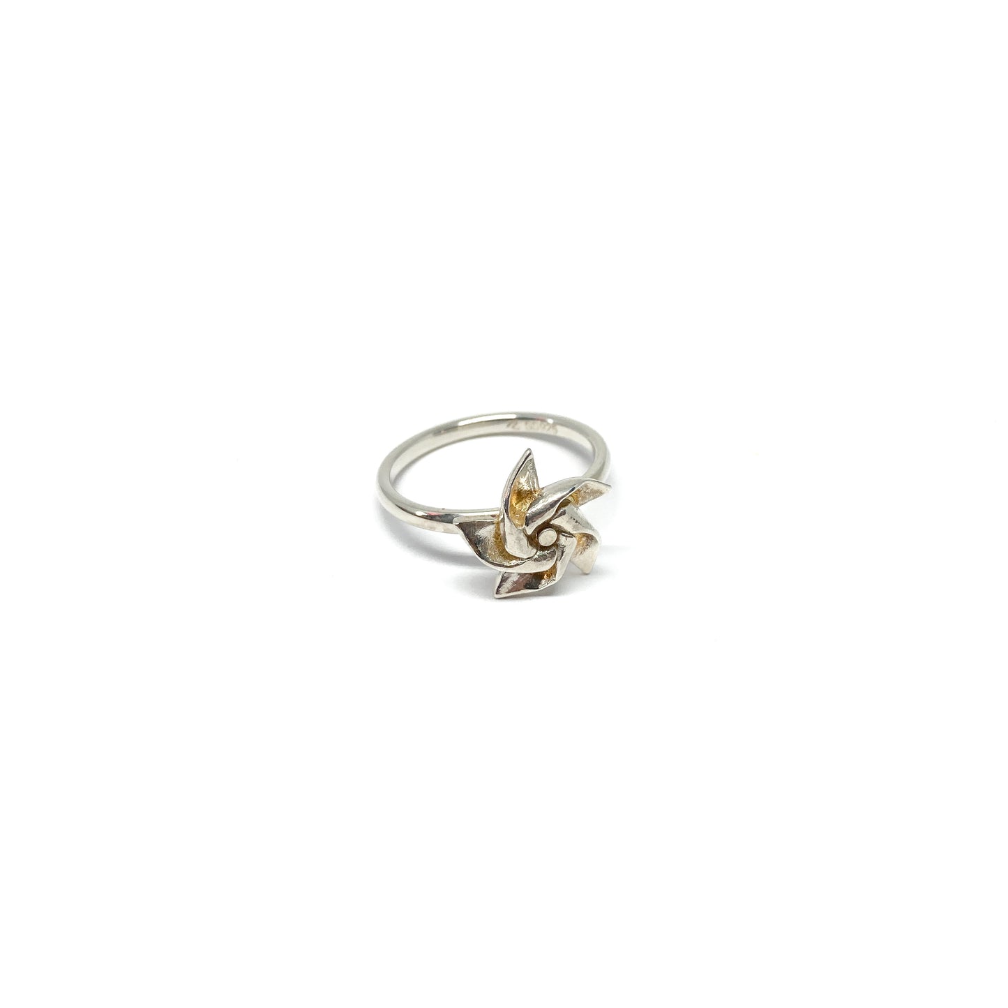 A shiny silver ring features a three-dimensional, stylized floral or pinwheel design as its centerpiece.